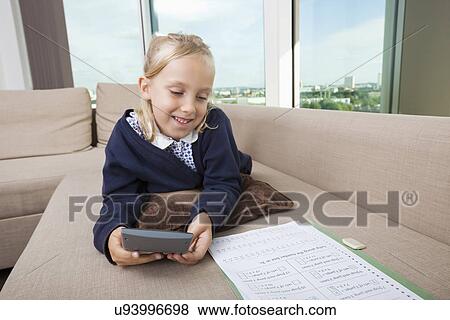 Stock Photo - Little girl using calculator while studying on sofa. Fotosearch