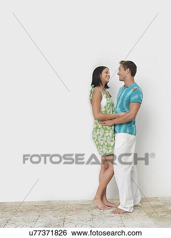 Stock Photograph - Loving young couple standing against wall. Fotosearch