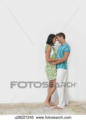 Stock Photography - Loving young couple standing together against wall. Fotosearch