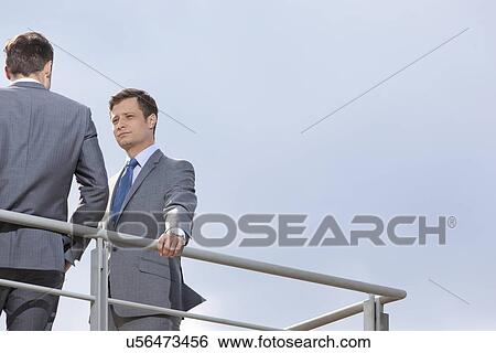 Low angle view of young businessman looking at coworker against clear sky View Large Photo Image Stock Photograph - Low angle view of young businessman looking at coworker against clear sky. Fotosearch