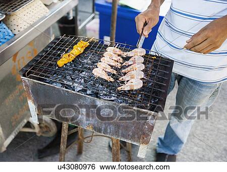Stock Photograph - Low section of young man cooking prawns on barbecue, Koh Pha Ngan, Thailand. Fotosearch