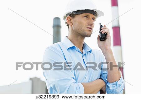 Male architect communicating on walkie-talkie at site View Large Photo Image Stock Photo - Male architect communicating on walkie-talkie at site. Fotosearch