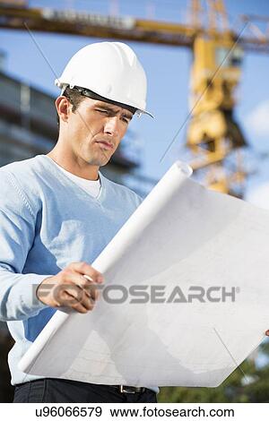 Male architect examining blueprint at construction site View Large Photo Image Stock Photo - Male architect examining blueprint at construction site. Fotosearch