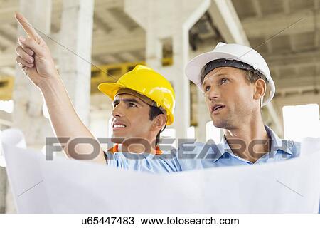 Male architect explaining building plan to colleague at construction site View Large Photo Image Stock Image - Male architect explaining building plan to colleague at construction site. Fotosearch
