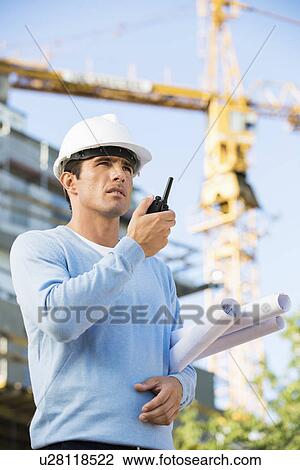 Male architect holding blueprints while using walkie-talkie at construction site View Large Photo Image Stock Image - Male architect holding blueprints while using walkie-talkie at construction site. Fotosearch
