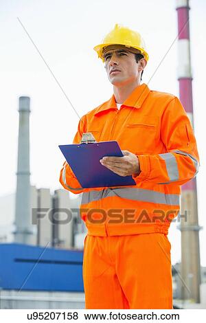 Male architect holding clipboard while standing at site View Large Photo Image Stock Photo - Male architect holding clipboard while standing at site. Fotosearch