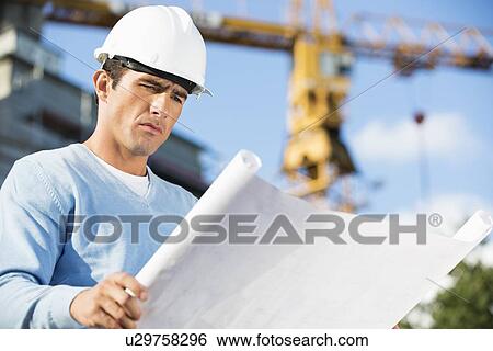 Stock Photograph - Male architect reviewing blueprint at construction site. Fotosearch