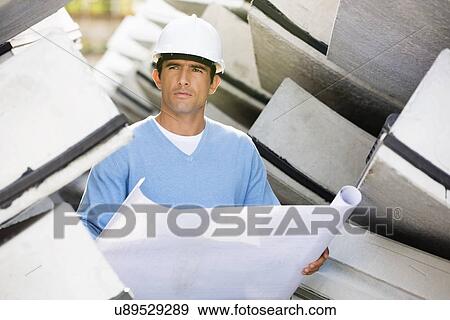 Male architect with blueprint working at construction site View Large Photo Image Stock Photo - Male architect with blueprint working at construction site. Fotosearch