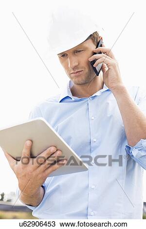 Male architect with digital tablet using cell phone at site View Large Photo Image Stock Image - Male architect with digital tablet using cell phone at site. Fotosearch
