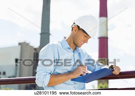 Stock Photography - Male architect writing on clipboard at site. Fotosearch