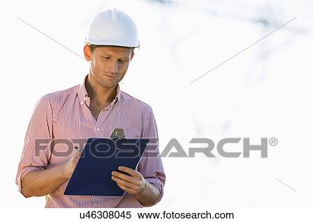 Male architect writing on clipboard at site View Large Photo Image Stock Photography - Male architect writing on clipboard at site. Fotosearch