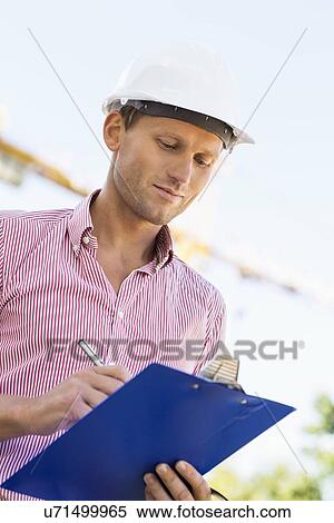 Male architect writing on clipboard at site View Large Photo Image Stock Photography - Male architect writing on clipboard at site. Fotosearch