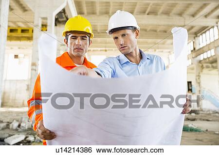Stock Photograph - Male architects discussing over blueprint at construction site. Fotosearch