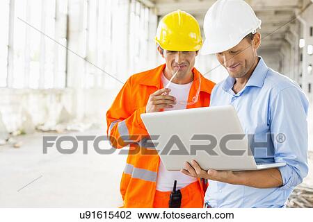 Stock Image - Male architects using laptop at construction site. Fotosearch