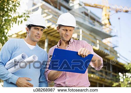 Stock Photo - Male architects with blueprint and clipboard working at site. Fotosearch