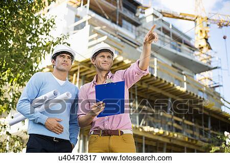 Stock Photo - Male architects with blueprint and clipboard working at site. Fotosearch
