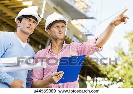 Stock Photo - Male architects with blueprint and clipboard working at site. Fotosearch