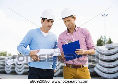 Stock Photograph - Male architects with blueprint and clipboard working at site. Fotosearch