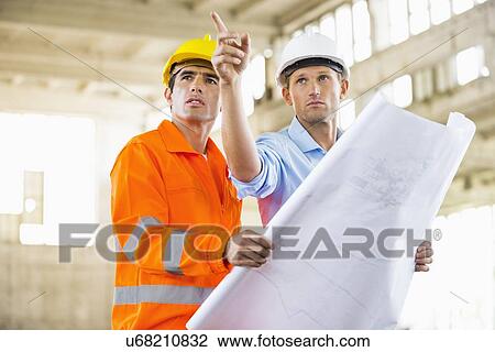 Male architects with blueprint working at construction site View Large Photo Image Stock Image - Male architects with blueprint working at construction site. Fotosearch
