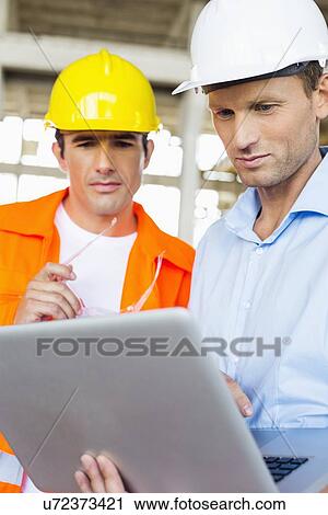 Male architects working on laptop at construction site View Large Photo Image Stock Image - Male architects working on laptop at construction site. Fotosearch