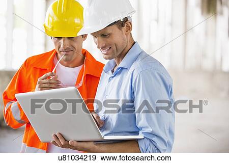 Male architects working on laptop at construction site View Large Photo Image Stock Photo - Male architects working on laptop at construction site. Fotosearch