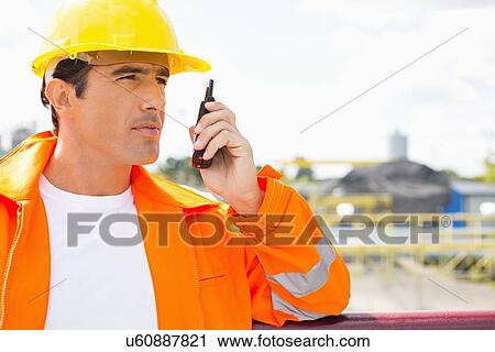 Stock Image - Male construction worker communicating on walkie-talkie at site. Fotosearch