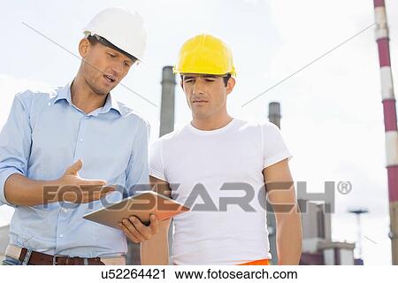 Male construction workers discussing over digital tablet at industry View Large Photo Image Stock Image - Male construction workers discussing over digital tablet at industry. Fotosearch