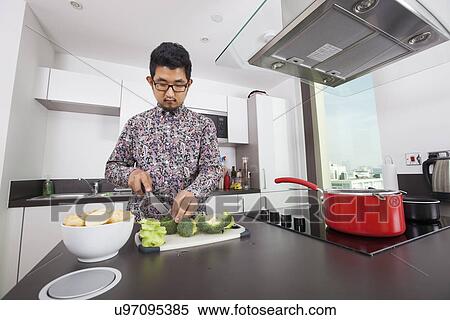 Stock Photography - Man cutting broccoli at kitchen counter. Fotosearch