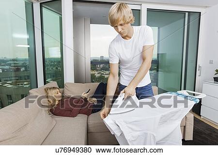 Man ironing shirt while woman relaxing on sofa at home View Large Photo Image Stock Image - Man ironing shirt while woman relaxing on sofa at home. Fotosearch