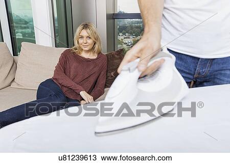 Man ironing shirt while woman relaxing on sofa at home View Large Photo Image Stock Image - Man ironing shirt while woman relaxing on sofa at home. Fotosearch