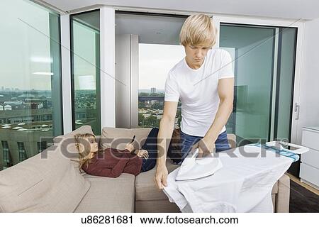 Man ironing shirt while woman relaxing on sofa at home View Large Photo Image Stock Image - Man ironing shirt while woman relaxing on sofa at home. Fotosearch