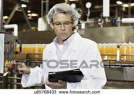 Stock Image - Man looking at tablet PC while working in bottling factory. Fotosearch
