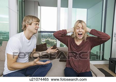 Stock Photography - Man trying to talk as woman yells out aloud in living room at home. Fotosearch