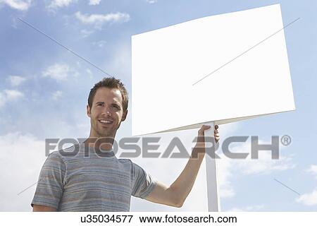 Man with standing by blank sign against cloudy sky View Large Photo Image Stock Photo - Man with standing by blank sign against cloudy sky. Fotosearch