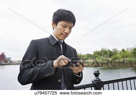 Mid adult Asian businessman using cell phone along river View Large Photo Image Stock Photography - Mid adult Asian businessman using cell phone along river. Fotosearch