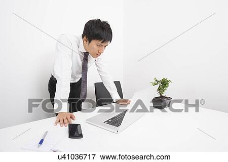 Mid adult businessman looking at laptop in office View Large Photo Image Stock Photo - Mid adult businessman looking at laptop in office. Fotosearch