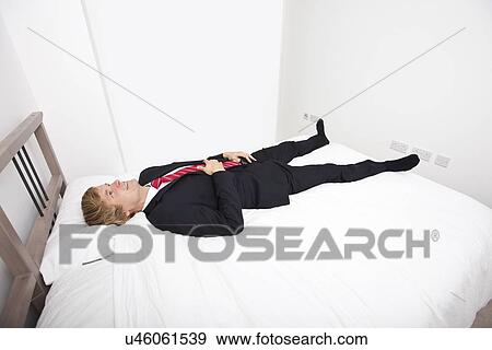 Stock Photo - Mid adult businessman lying in bed at home. Fotosearch