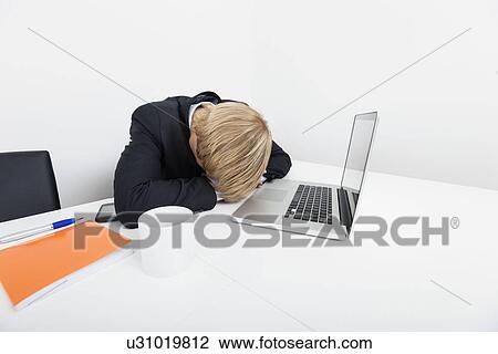 Stock Image - Mid adult businessman sleeping by laptop at desk in office. Fotosearch