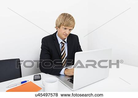 Mid adult businessman using laptop at desk in office View Large Photo Image Stock Photo - Mid adult businessman using laptop at desk in office. Fotosearch