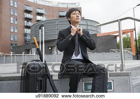 Mid adult businessman with luggage adjusting necktie against buildings View Large Photo Image Stock Image - Mid adult businessman with luggage adjusting necktie against buildings. Fotosearch