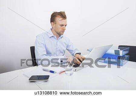 Mid-adult businessman working on laptop at desk in office View Large Photo Image Stock Image - Mid-adult businessman working on laptop at desk in office. Fotosearch