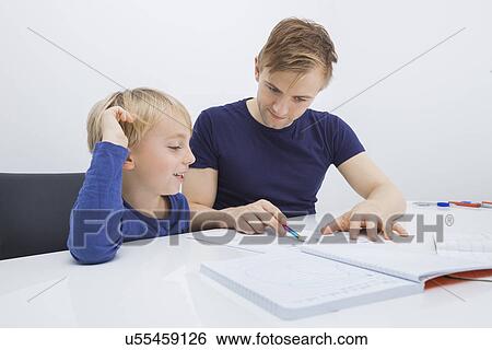 Stock Photograph - Mid adult man assisting boy in studies at table. Fotosearch