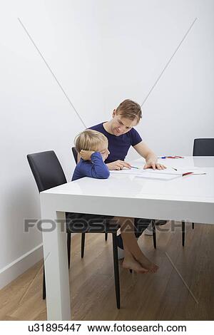 Stock Photo - Mid adult man helping boy in studies at table. Fotosearch