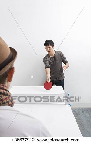 Stock Image - Mid adult man playing table tennis with friend. Fotosearch
