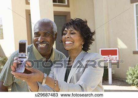 Stock Image - Middle-aged couple photographing in front of new home. Fotosearch