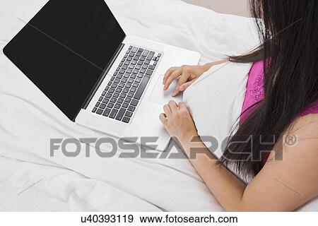 Midsection of woman using laptop on bed View Large Photo Image Stock Photo - Midsection of woman using laptop on bed. Fotosearch