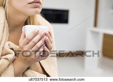 Stock Image - Midsection of young woman holding coffee mug in house. Fotosearch