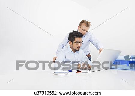 Stock Image - Multiethnic businessmen working on laptop at desk in office. Fotosearch
