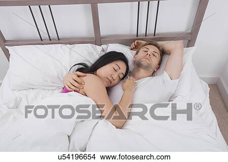 Picture - Multiethnic couple sleeping in bed. Fotosearch