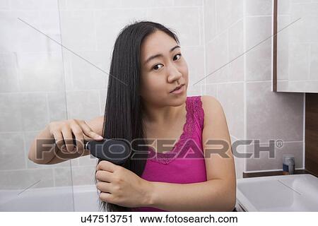 Stock Image - Portrait of Asian woman brushing her hair in bathroom. Fotosearch